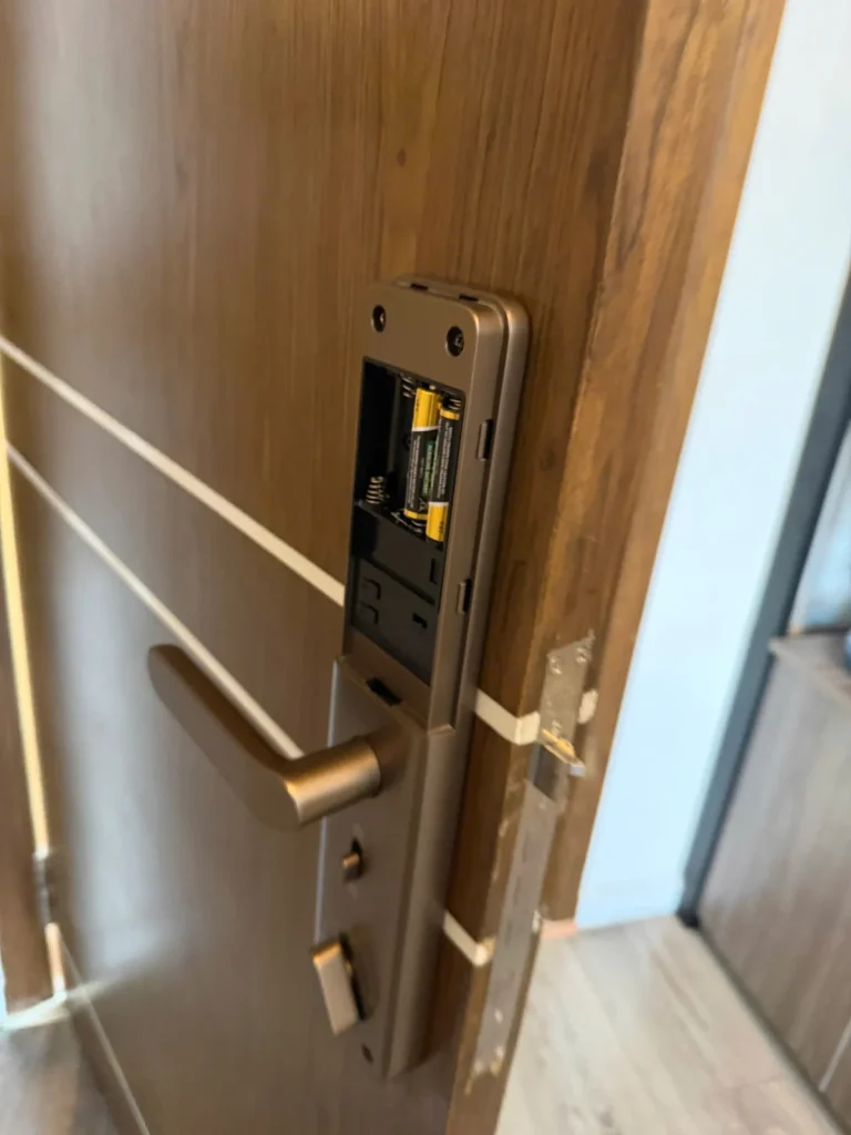 Khóa điện tử màu đồng trên cửa gỗ, nắp khoang pin mặt trong đang mở