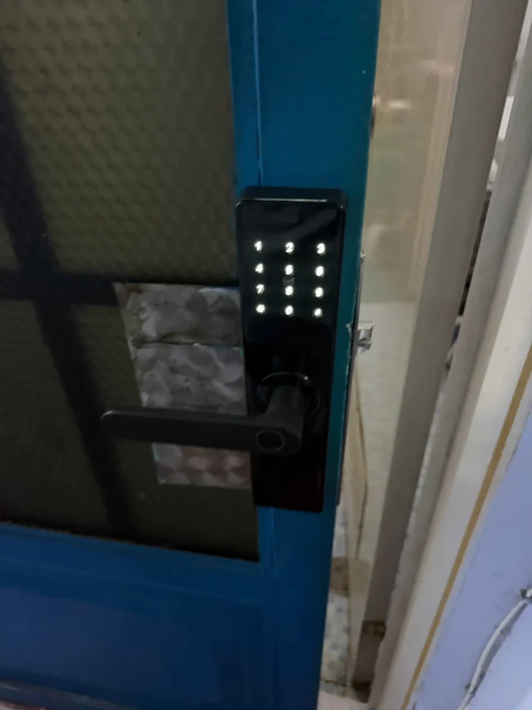 Khóa mã số bàn phím sáng trắng lắp trên cửa kính khung xanh
